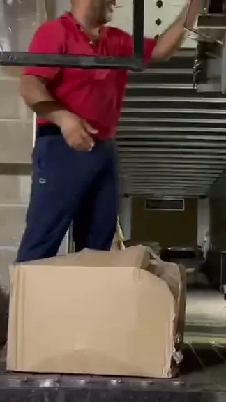 A hub worker in a red shirt loads a crushed, split-open carton onto a belt, its contents bagged in plastic beside him.