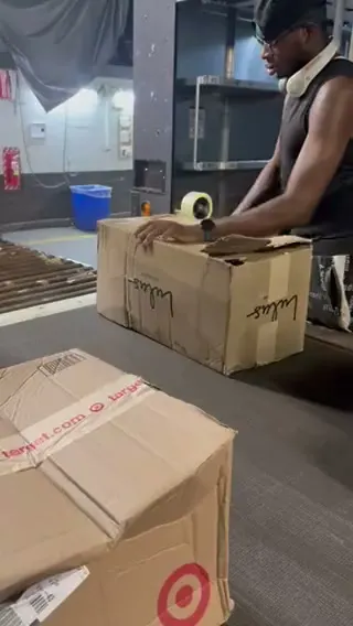 A hub worker runs a tape gun across the top of a carton that has split open on the belt, with re-taped boxes stacked in front of him.