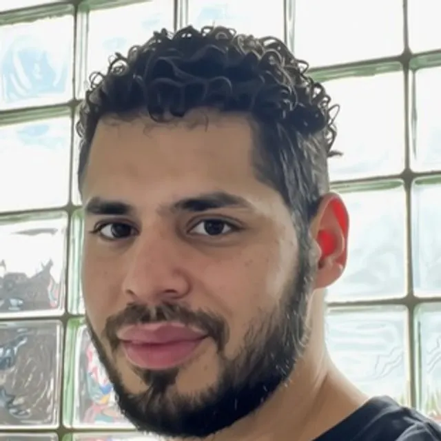 Luis Triolet in a black Teamsters shirt, in front of a glass-block window.